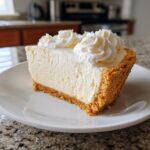 A decadent slice of white chocolate mousse tart with a graham cracker crust, topped with whipped cream swirls.