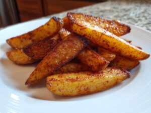 A close-up of golden brown, seasoned air fryer potato wedges piled on a white plate.