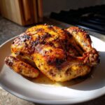 A perfectly cooked, golden-brown air fryer whole chicken resting on a white plate, showing crispy skin.