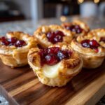 Close-up of freshly baked brie bites with melted cheese oozing out and topped with dark red cranberries.
