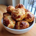 A white bowl filled with freshly baked, golden brown pretzel bites sprinkled generously with coarse salt.