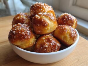 A white bowl filled with freshly baked, golden brown pretzel bites sprinkled generously with coarse salt.