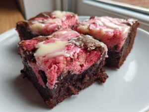 Three rich, fudgy strawberry brownies with a pink layer and white drizzle on a white plate.
