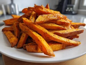A close-up of a large pile of golden, seasoned sweet potato fries stacked high on a white plate.