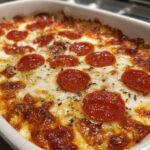 Close-up of a bubbly, baked pepperoni pizza dip topped with melted cheese and herbs in a white dish.
