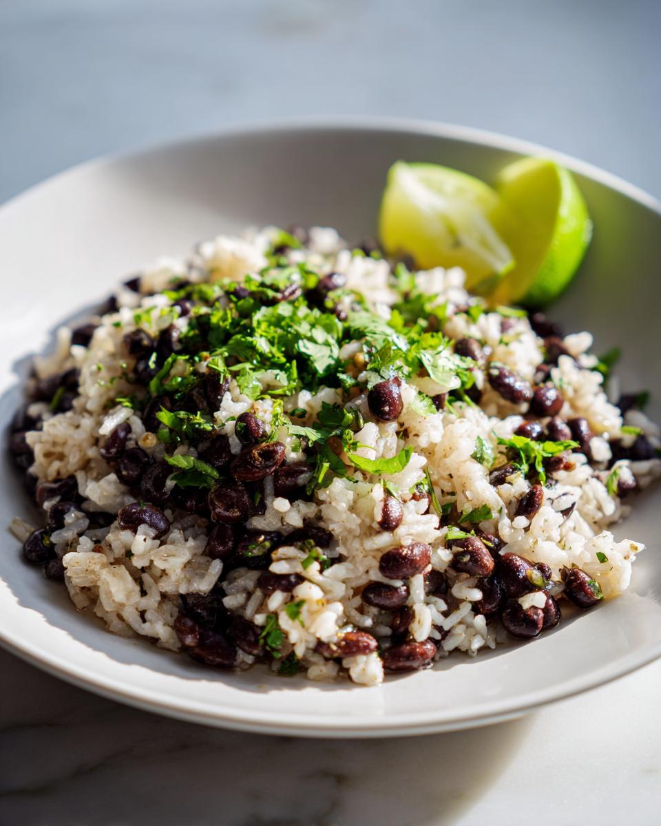 A close-up of a serving of flavorful black beans and rice topped with fresh cilantro and lime wedges.