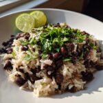 A close-up of a bowl of flavorful black beans and rice, topped with fresh cilantro and garnished with lime wedges.
