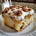 A close-up of a moist slice of butter pecan praline poke cake topped with white frosting and candied pecans.