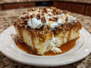 A moist slice of butter pecan praline poke cake topped with whipped cream, caramel sauce, and chopped pecans.