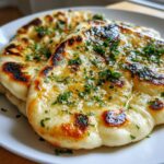 Two pieces of freshly cooked naan bread, brushed with melted butter and topped with chopped parsley.