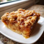 A close-up of a square slice of caramel apple dump cake with a thick, gooey caramel topping and crumbly streusel.