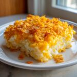 A square serving of cheesy potato bake topped with melted cheddar and crispy cornflakes on a white plate.