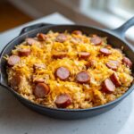 Close-up of cheesy sausage and rice cooked in a black cast iron skillet, topped with melted cheddar.