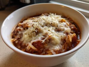 Close-up of a bowl of rich tomato-based chicken parmesan soup topped with melted mozzarella and herbs.