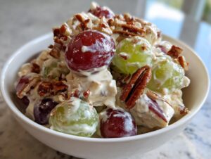 A close-up of creamy chicken salad chick grape salad mixed with red and green grapes and topped with pecans.