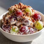 A creamy bowl of chicken salad chick grape salad featuring red and green grapes coated in dressing and topped with chopped pecans.