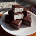 A stack of chocolate-covered cool whip candy pieces, two of which are cut in half showing the fluffy white center.