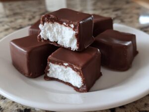 Close-up of several chocolate-coated squares revealing a fluffy white cool whip candy center.