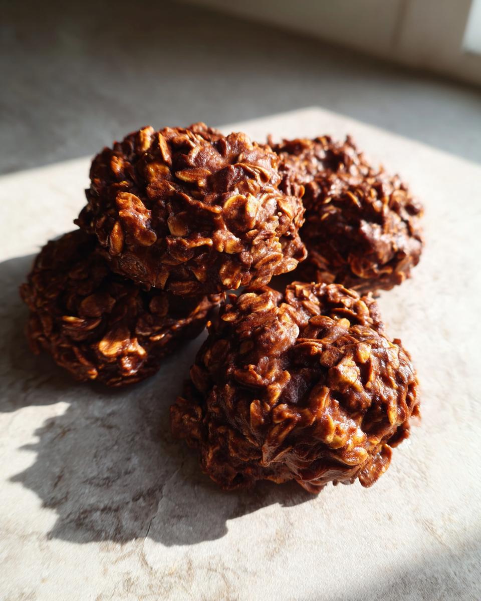 A stack of four rich, chocolatey no bake cookies studded with visible oats, resting on a light surface.