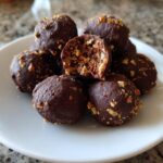 A pile of rich, chocolate-covered pecan pie balls, one of which is broken open revealing the nutty interior.