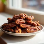 A close-up of a pile of freshly made cinnamon sugar pecans glistening with sugar crystals on a small white plate.