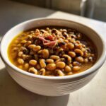 A close-up of a white bowl filled with creamy black eyed peas and a piece of ham.