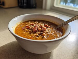 A white bowl filled with creamy black eyed peas stew topped with ham and cheese, ready to eat.