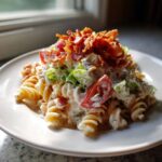 A serving of creamy blt pasta salad with fusilli pasta, tomatoes, lettuce, and topped with crispy bacon.