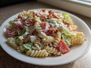 A close-up of a serving of creamy blt pasta salad featuring rotini pasta, lettuce, tomatoes, and crumbled bacon.