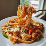 A fork lifts a generous portion of creamy Cajun chicken pasta, coated in sauce and cheese, from a white plate.