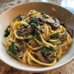 A close-up of creamy mushroom pasta tossed with wilted spinach and topped with Parmesan cheese.