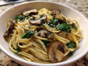 Close-up of creamy mushroom pasta tossed with sautéed spinach and topped with sliced mushrooms.