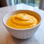 A close-up of thick, vibrant orange nacho cheese sauce swirled inside a small, white, ribbed ramekin.
