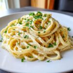 Close-up of a serving of creamy parmesan pasta tossed in a rich white sauce and topped with chopped fresh parsley.
