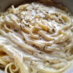 Close-up of spaghetti noodles generously coated in rich, creamy homemade alfredo sauce and sprinkled with dried herbs.