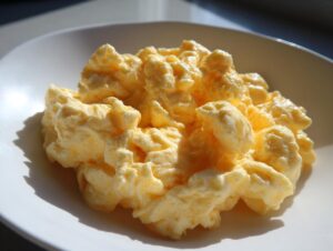 Close-up of very creamy, soft scrambled eggs piled high on a white plate, glistening in the light.
