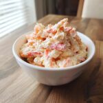 A white bowl filled high with creamy seafood salad featuring visible chunks of pink/orange seafood.