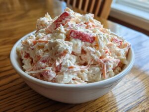 A close-up shot of a generous serving of creamy seafood salad, featuring white and red chunks, in a white bowl.
