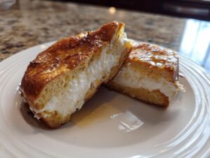 Two halves of golden brown stuffed french toast filled with white cream cheese, drizzled with syrup.