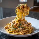 A fork lifting a large twirl of crockpot garlic parmesan chicken pasta, topped with cheese and herbs.