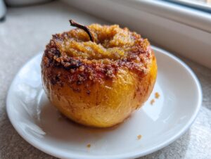A single, golden-brown baked apples dessert served on a small white plate, featuring a caramelized, sugary topping.