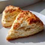 Two perfectly baked, triangular scones showing flaky layers and a golden crust, ready to eat.
