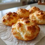 Five golden-brown, fluffy cloud bread buns resting on parchment paper.