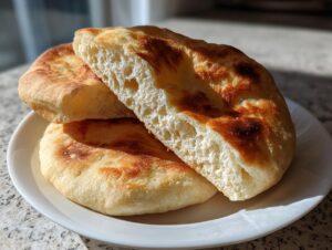 Close-up of fluffy, golden-brown homemade pita bread, one piece split open showing the airy interior.
