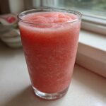 Close-up of a tall glass filled with a perfectly blended, icy strawberry daiquiri, condensation visible on the glass.