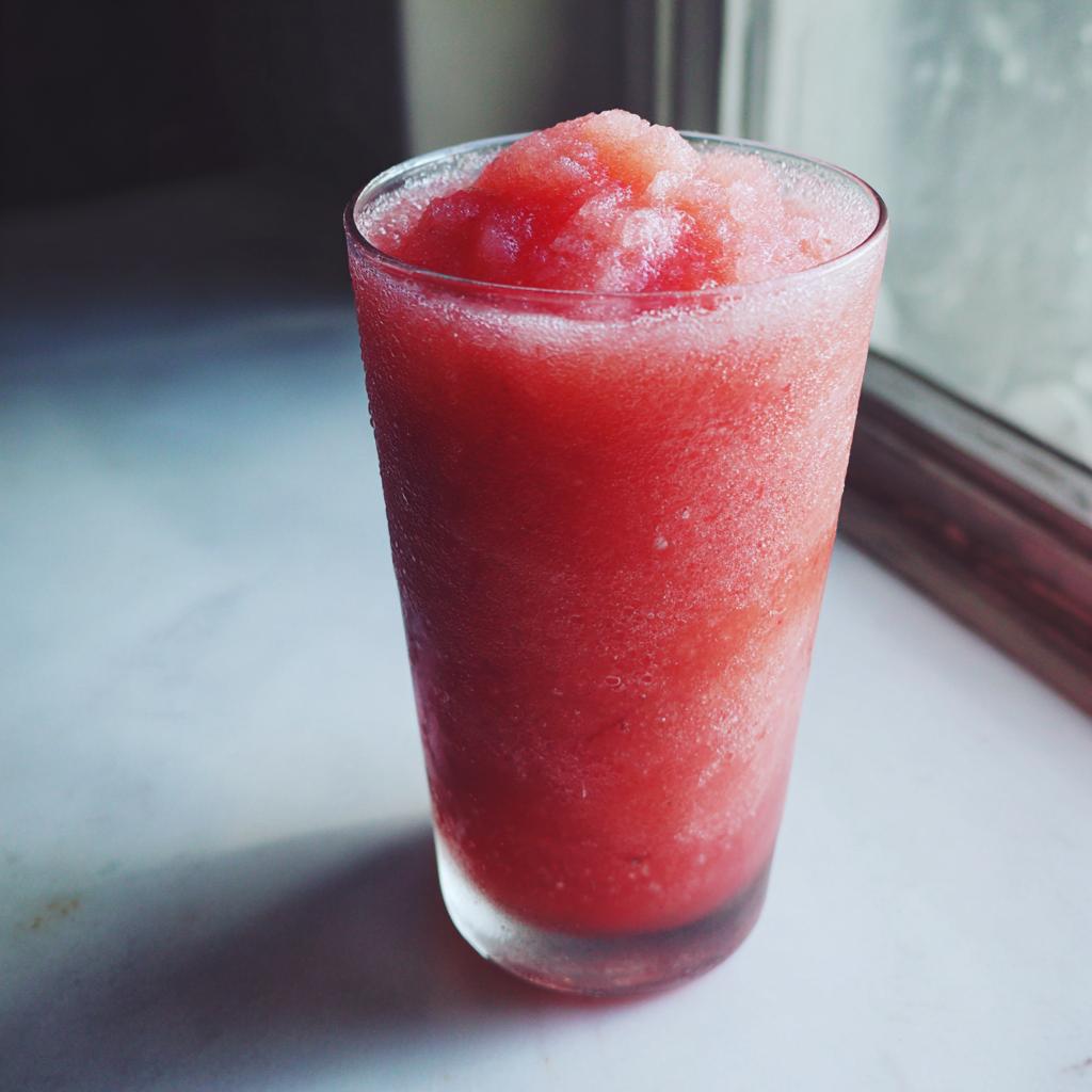 Close-up of a frosty, vibrant red strawberry daiquiri served in a tall glass, condensation visible on the exterior.