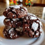 A stack of four rich, fudgy chocolate crinkle cookies dusted heavily with powdered sugar.