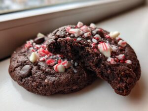 Two fudgy chocolate peppermint cookies topped with crushed candy canes and white chocolate chips.