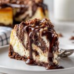 A rich slice of German chocolate cheesecake drizzled with chocolate sauce and topped with pecans.