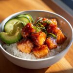 Close-up of glazed salmon cubes served over white rice with avocado and cucumber in salmon bowls.